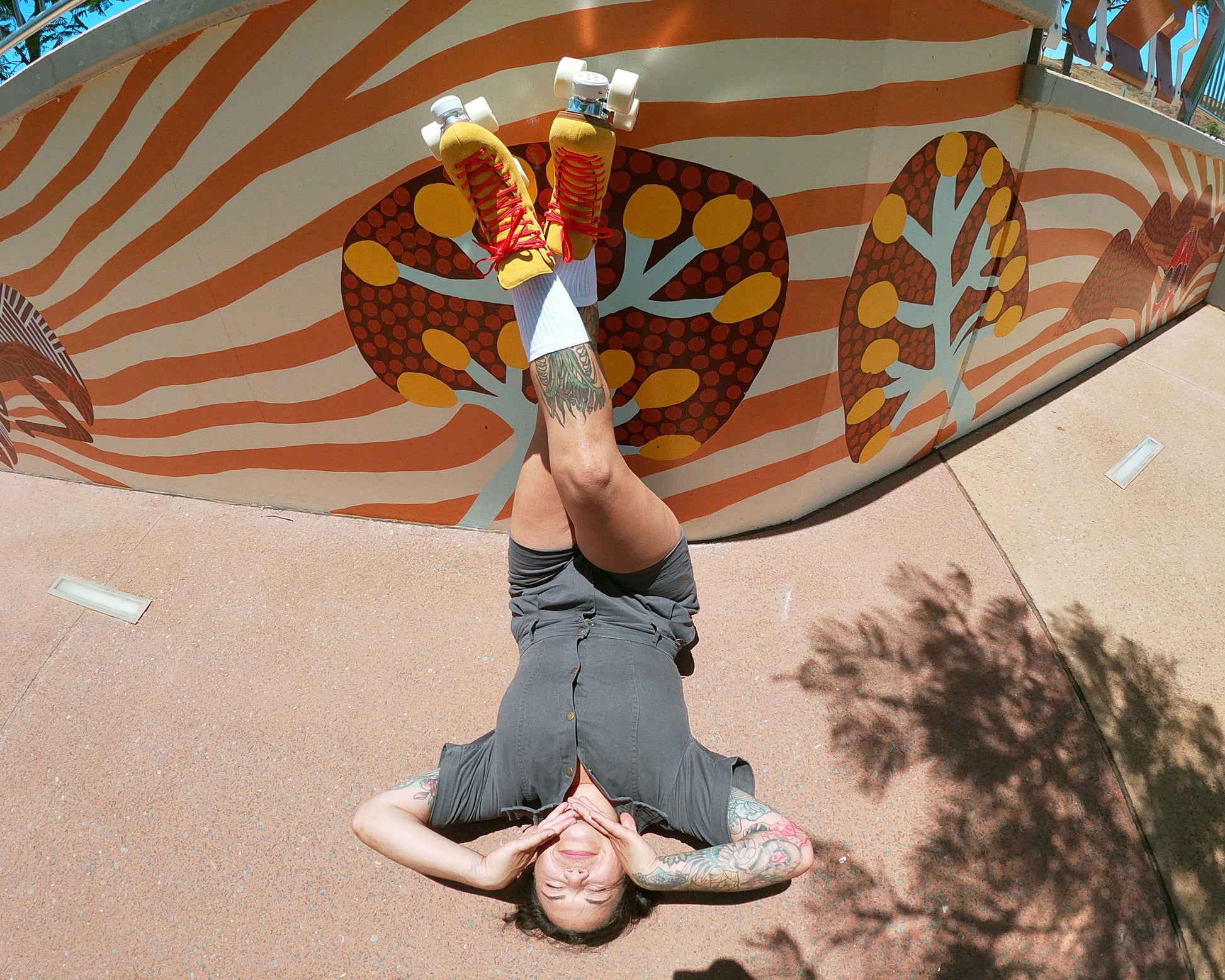roller skater laying on her back with legs crossed wearing Chuffed Skates yellow roller skates with aboriginal painting wall behind